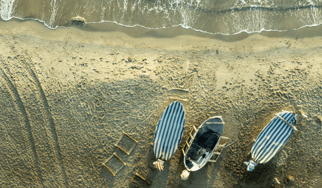 Three boats with stripped covers on a beach as the tide comes in | The Italian On Tour