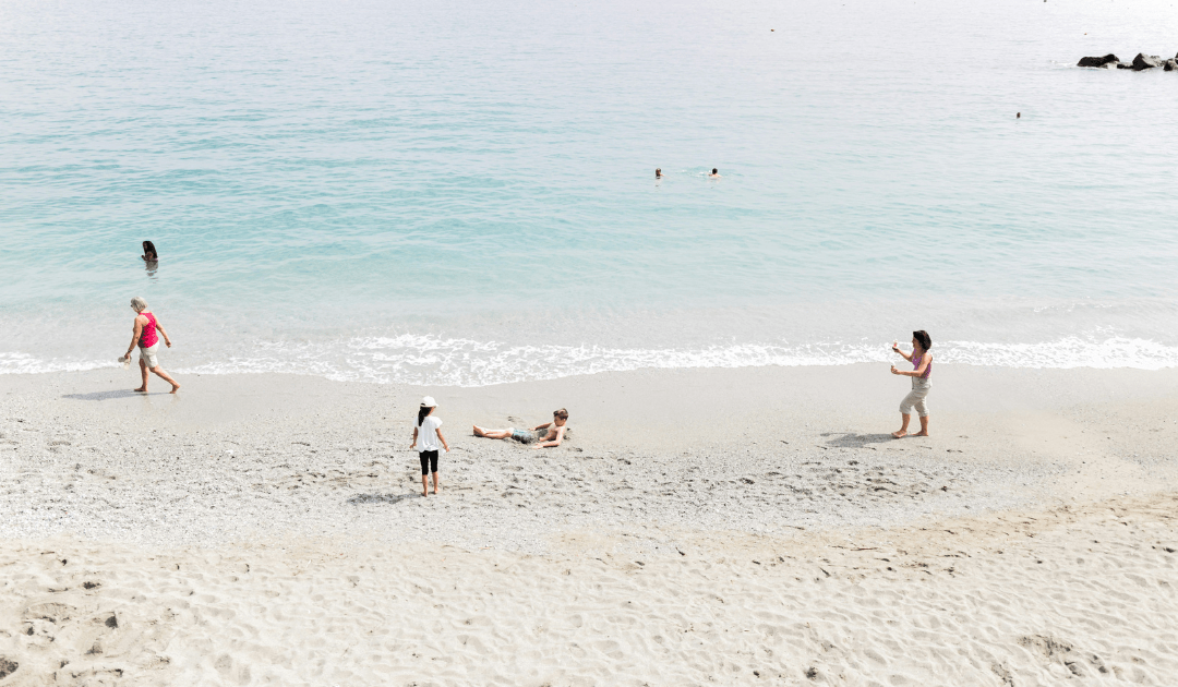 A Family playing on a white sand beach with clear water | The Italian On Tour