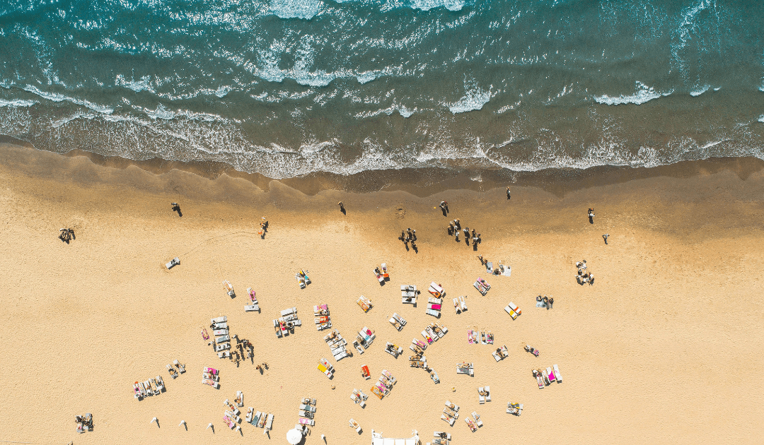 Overhead view of people on a golden sand beach with bright blue water | The Italian On Tour