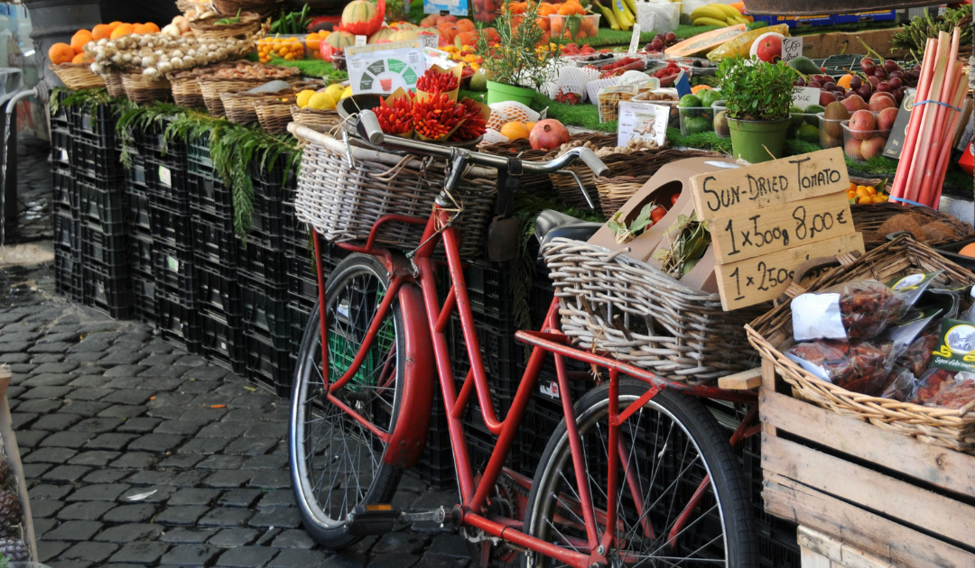 A red bike propped against a fruit and vegetable stand on a cobblestone street in Umbria